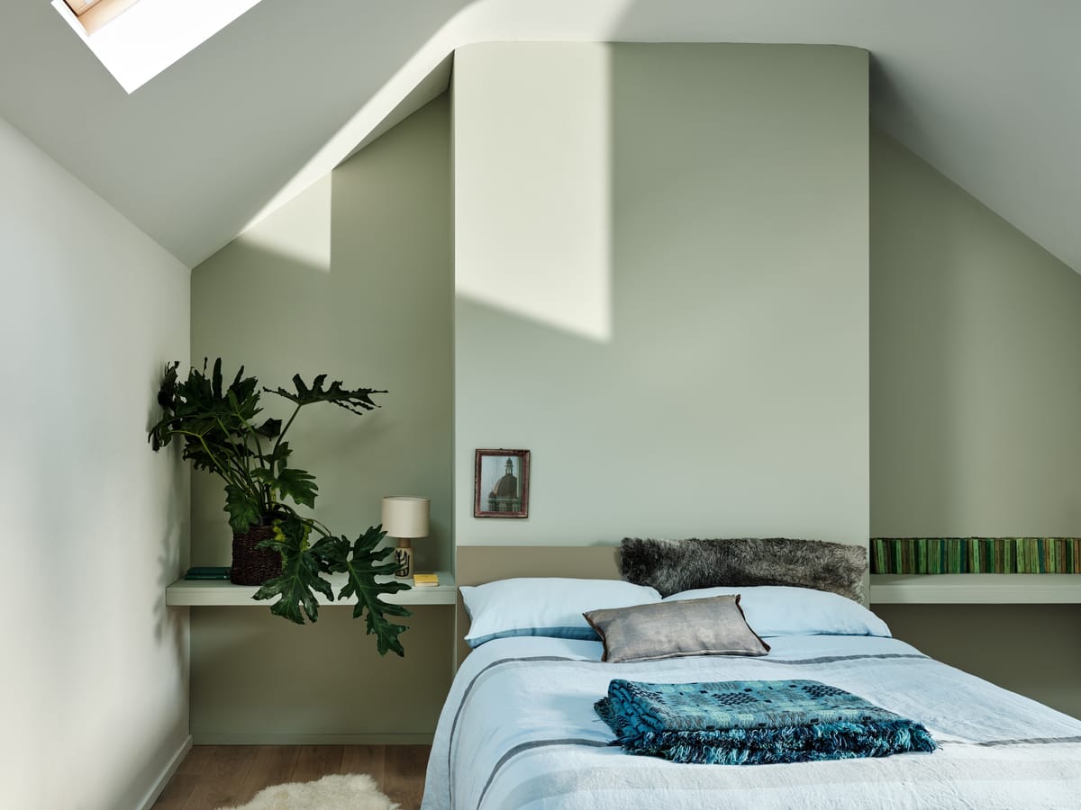 Wohnzimmer mit grünem Sofa, heller Wandfläche und Pendelleuchte